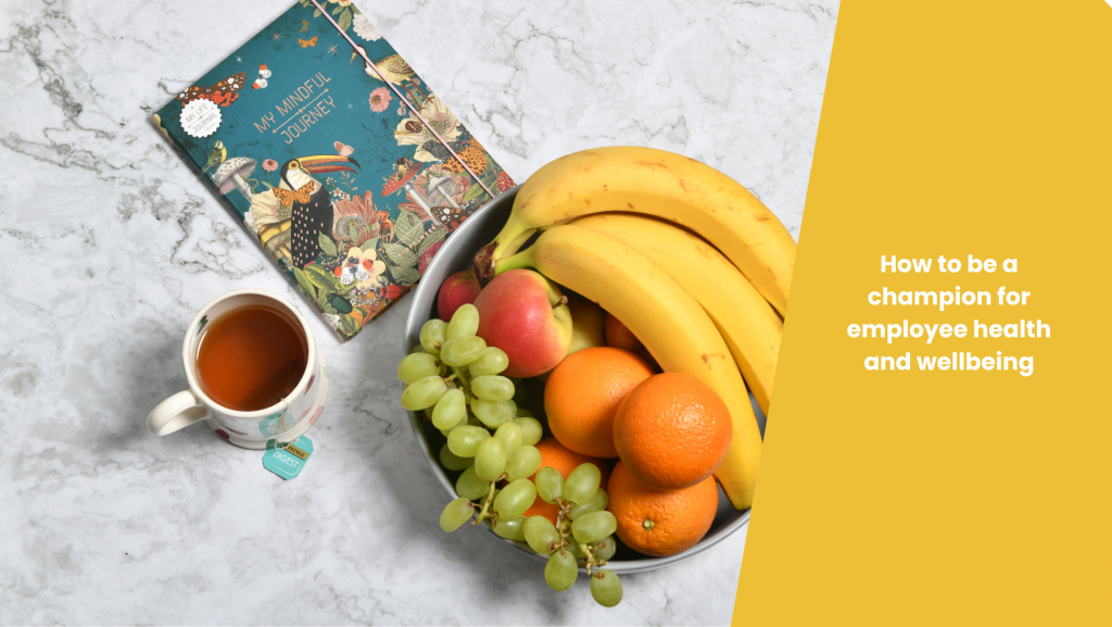 Flatlay showing colourful fruitbowl, tea, and mindfulness journal, with blog title 'How to be a champion for employee wellbeing ' written on yellow background