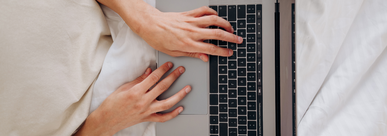 hands poised over laptop, typing on keyboard while under blanket