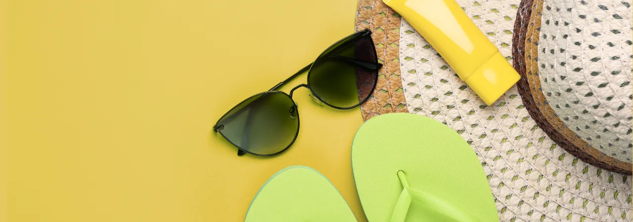 A flatlay image of Sunglasses, green flip flips, yellow sun cream bottle and sun hat, infront of yellow background